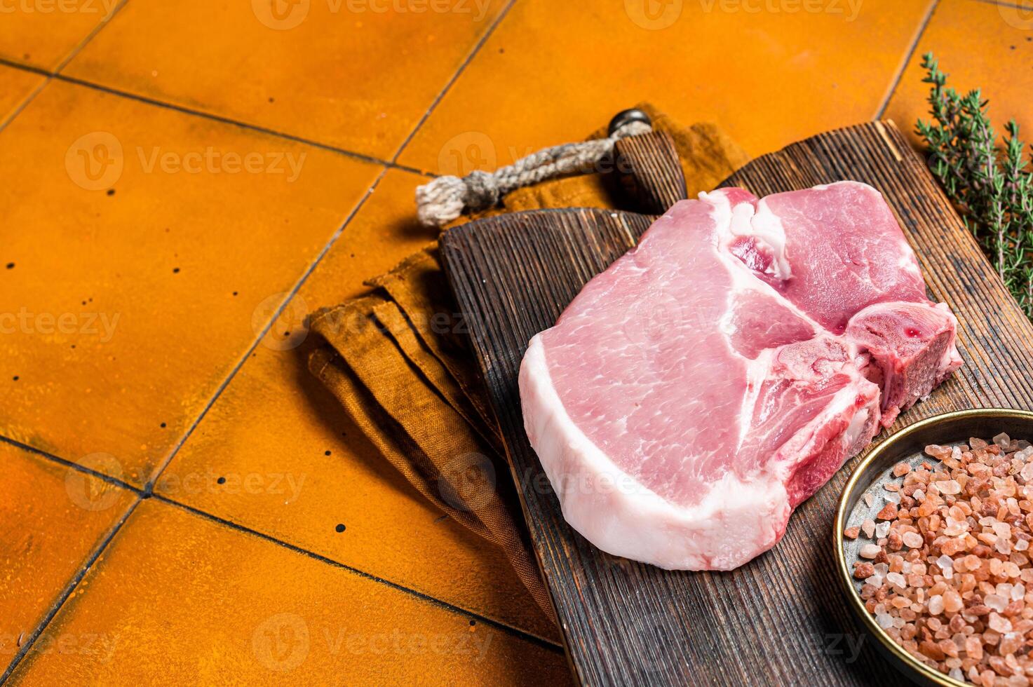 Fresh Raw pork t-bone chop meat steak on cutting board. Orange background. Top view. Copy space photo