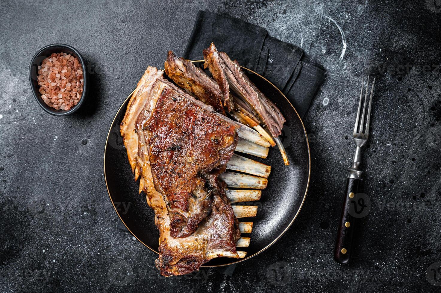 Roasted Rack of lamb ribs, mutton spareribs, sliced meat on plate. Black background. Top view photo
