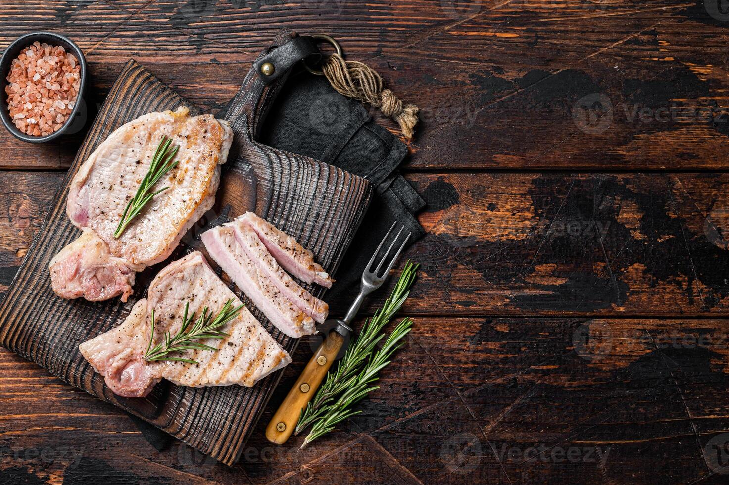 BBQ grilled pork chop steaks or cutlets sliced on wooden cutting board. Wooden background. Top view. Copy space photo