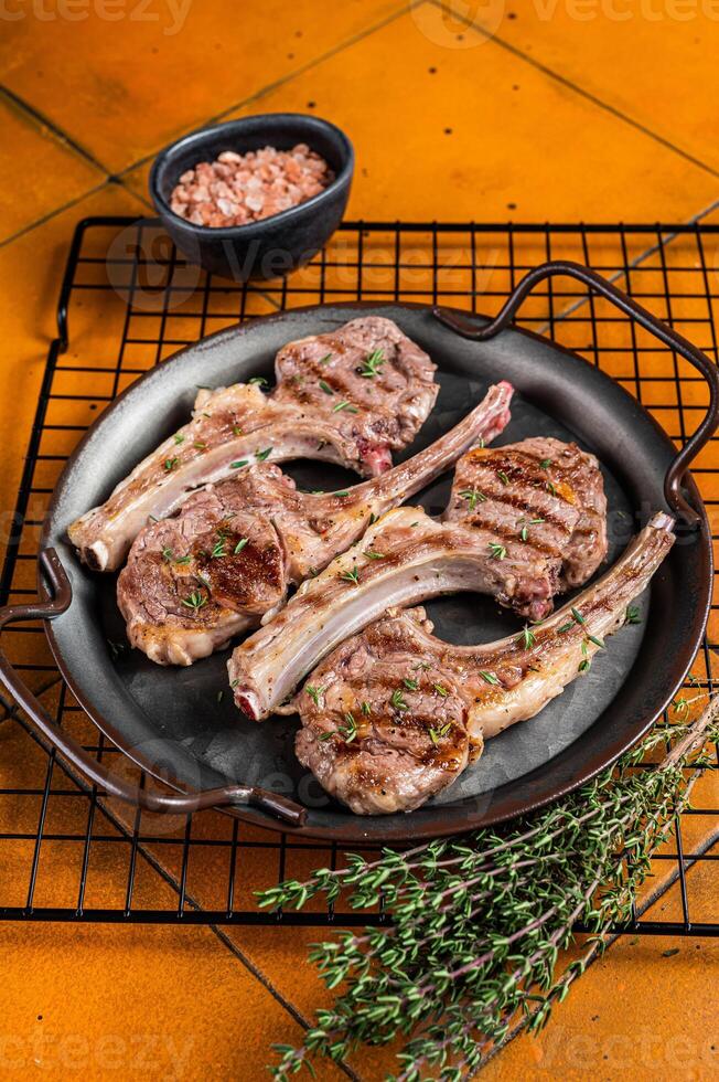 BBQ with Grilled lamb meat chops, mutton steaks with herbs. Orange background. Top view photo