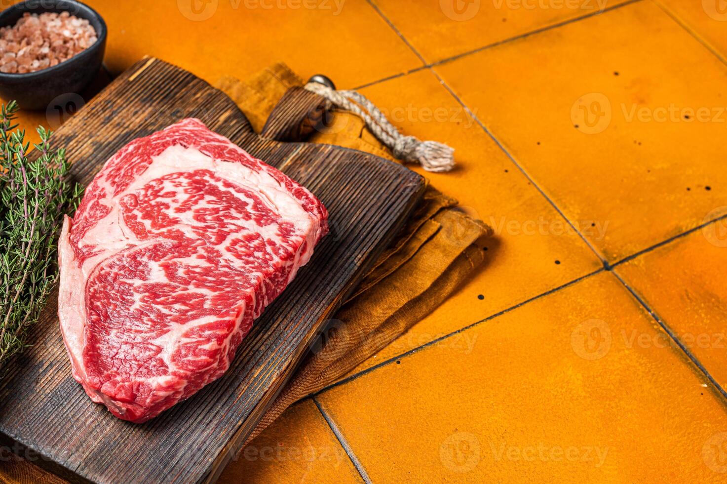 Prime Raw wagyu Rib Eye beef meat steak on wooden board. Orange background. Top view. Copy space photo
