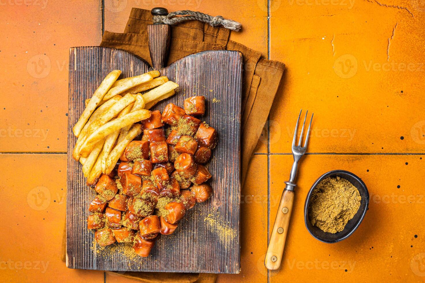 Curried sausage currywurst meal, curry wurst with french fry served on a wooden board. Orange background. Top view photo