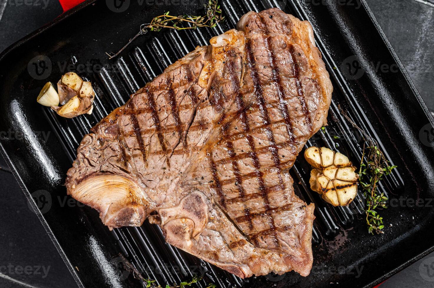 Grilled T-bone, t bone beef meat Steak on a grill skillet. Black background. Top view photo