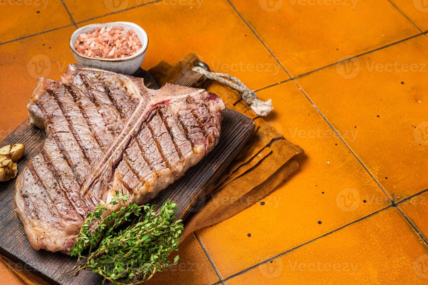 BBQ Roast T bone or Porterhouse beef meat Steak on a wooden board with spices. Orange background. Top view. Copy space photo