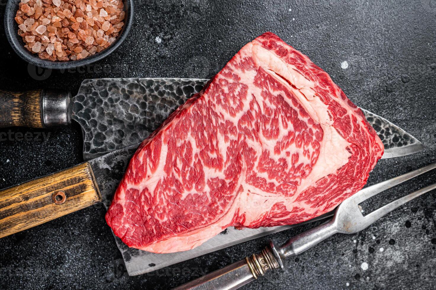 Butcher table with wagyu Rib Eye steak, raw beef meat. Black background. Top view photo