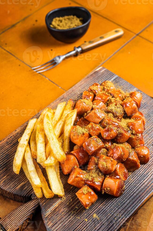 Curried sausage currywurst meal, curry wurst with french fry served on a wooden board. Orange background. Top view photo