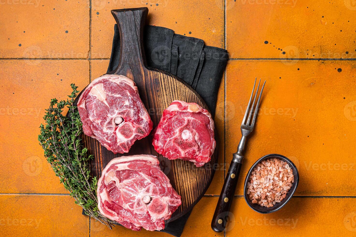 Raw lamb neck chops, fresh mutton meat on a butcher board with herbs. Orange background. Top view photo