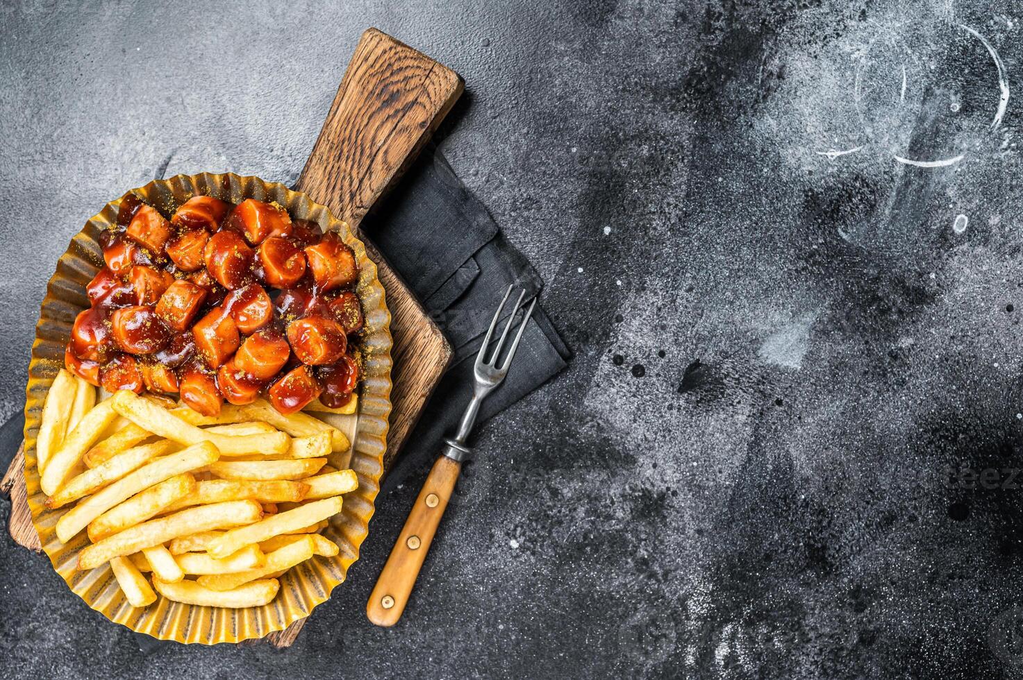 German currywurst with french fry served in a steel plate. Black background. Top view. Copy space photo