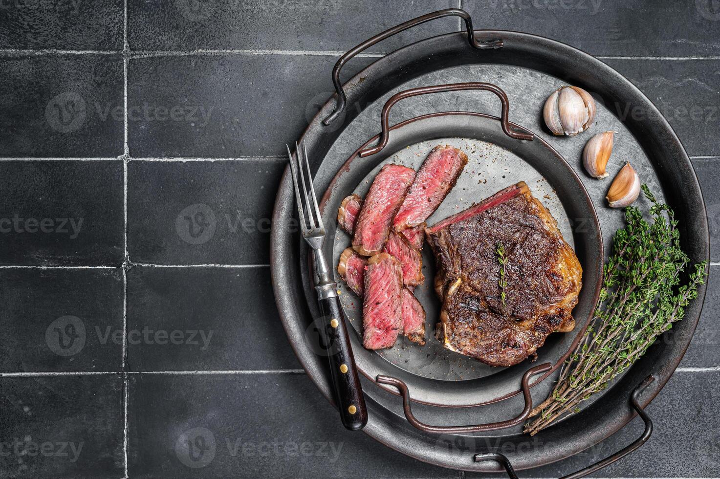 Roasted Sliced Wagyu New York beef meat steak or Striploin steak in a steel tray with herbs. Black background. Top view. Copy space photo