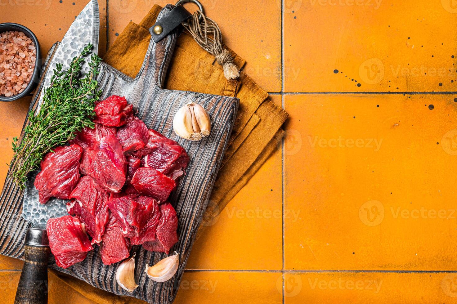 Raw beef meat chopped in cubes on wooden cutting board for cooking stew. Orange background. Top view. Copy space photo