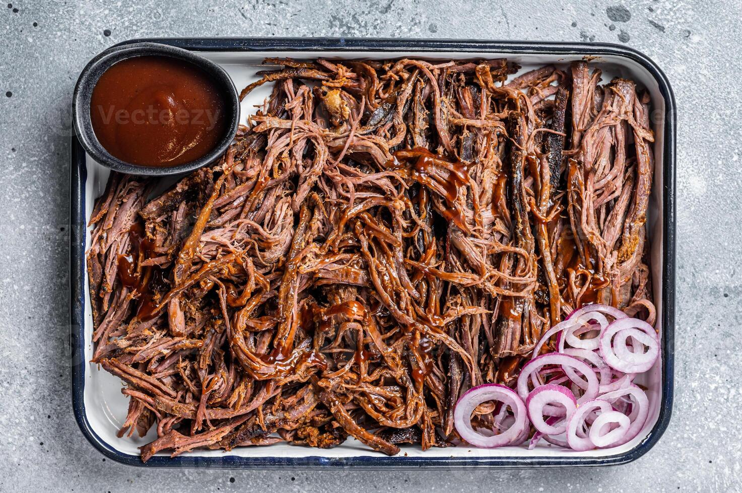 Pulled beef meat with hot chili sauce in baking dish. Gray background. Top view photo