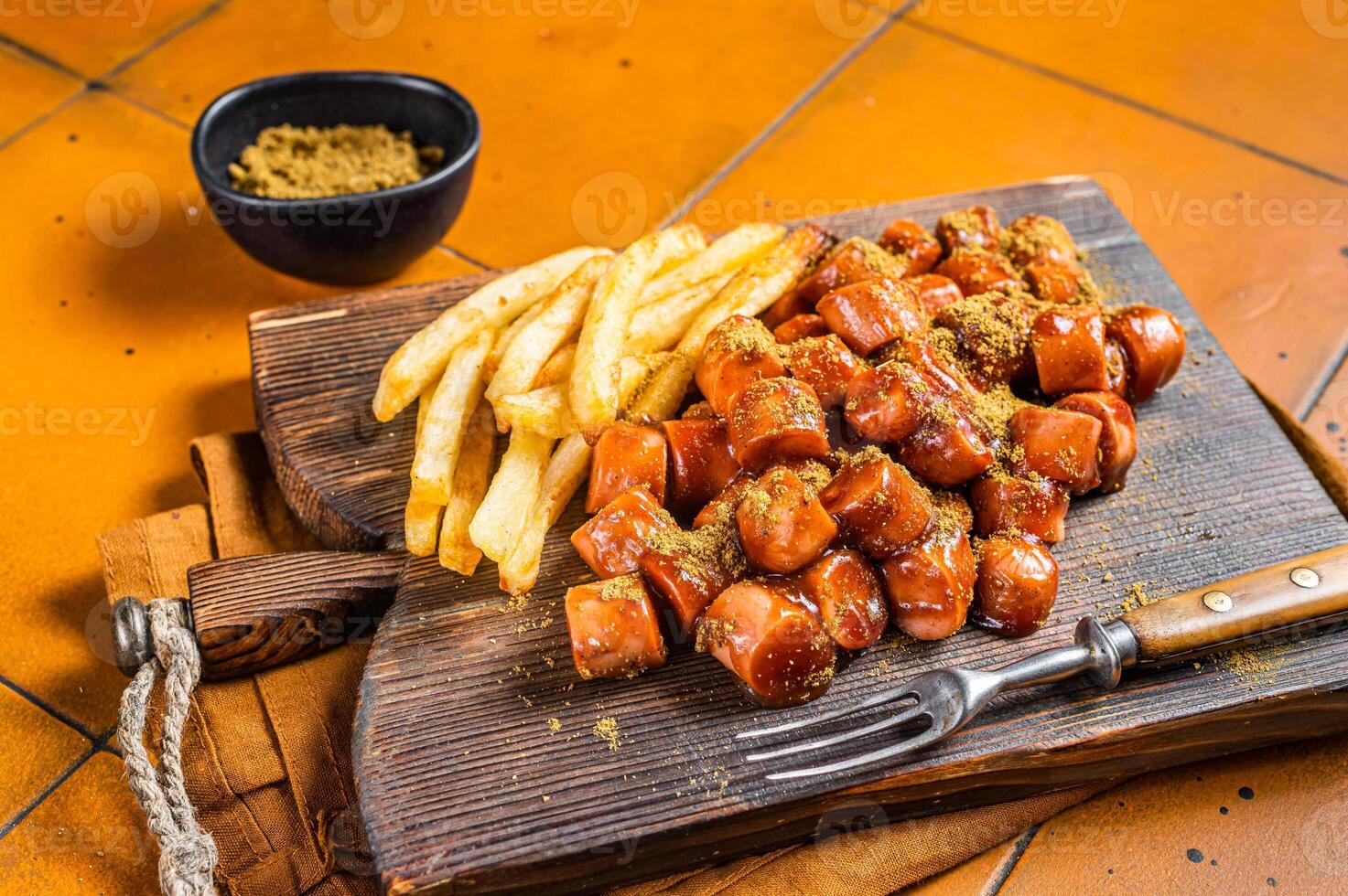 Curried sausage currywurst meal, curry wurst with french fry served on a wooden board. Orange background. Top view photo