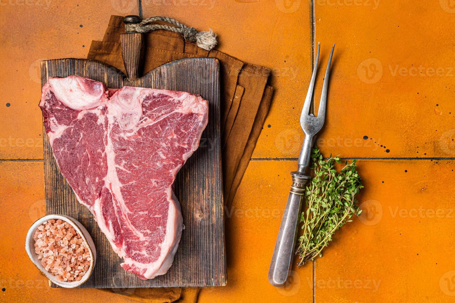 Porterhouse raw beef meat Steak, T-bone with thyme and sea salt on a wooden board. Orange background. Top view photo