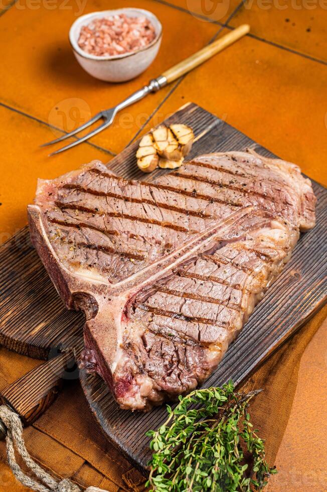 BBQ Roast T bone or Porterhouse beef meat Steak on a wooden board with spices. Orange background. Top view photo