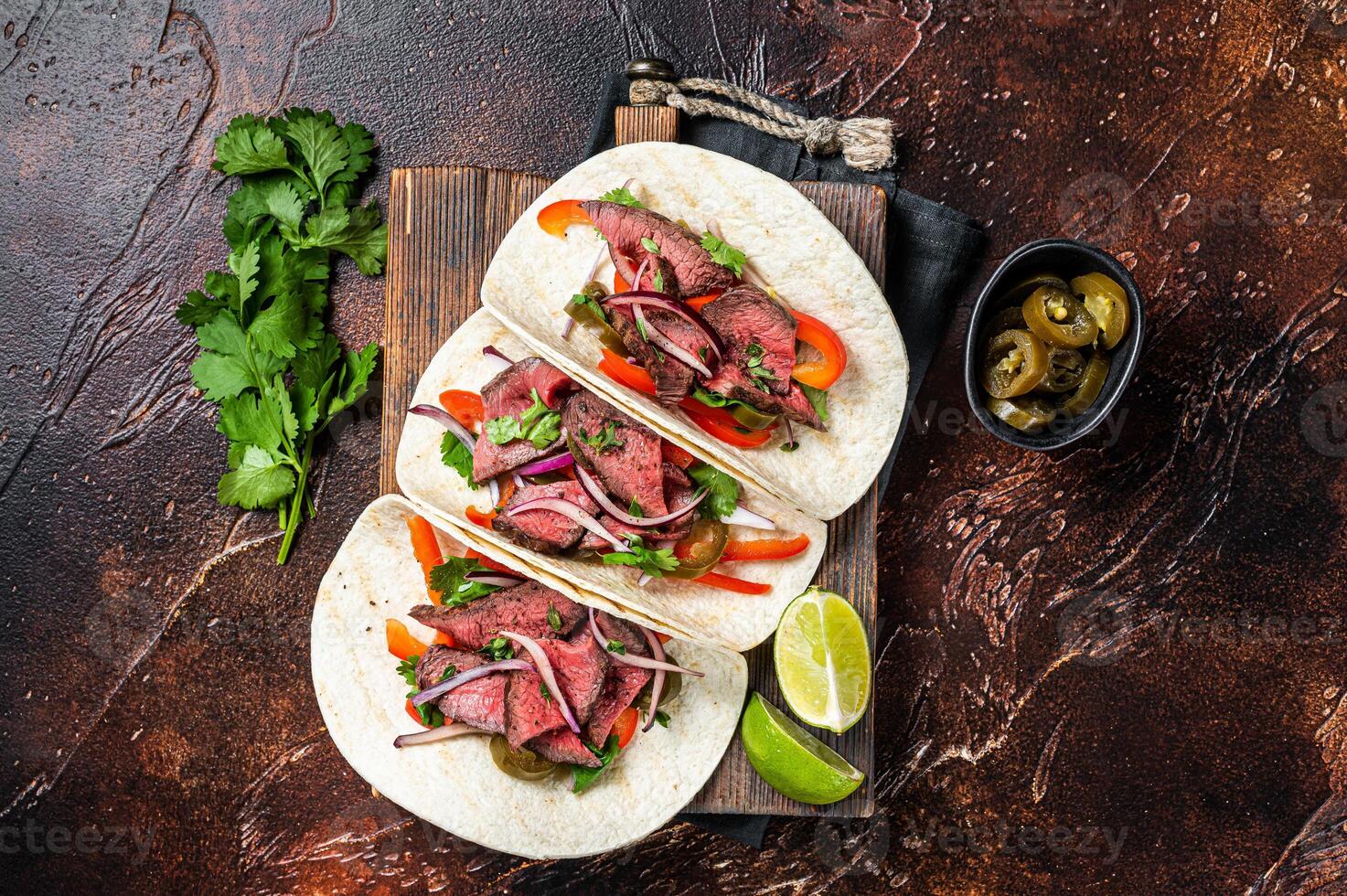 Carne Asada Tacos with grilled steak, green sauce, jalapenos and onion, Mexican food. Dark background. top view photo