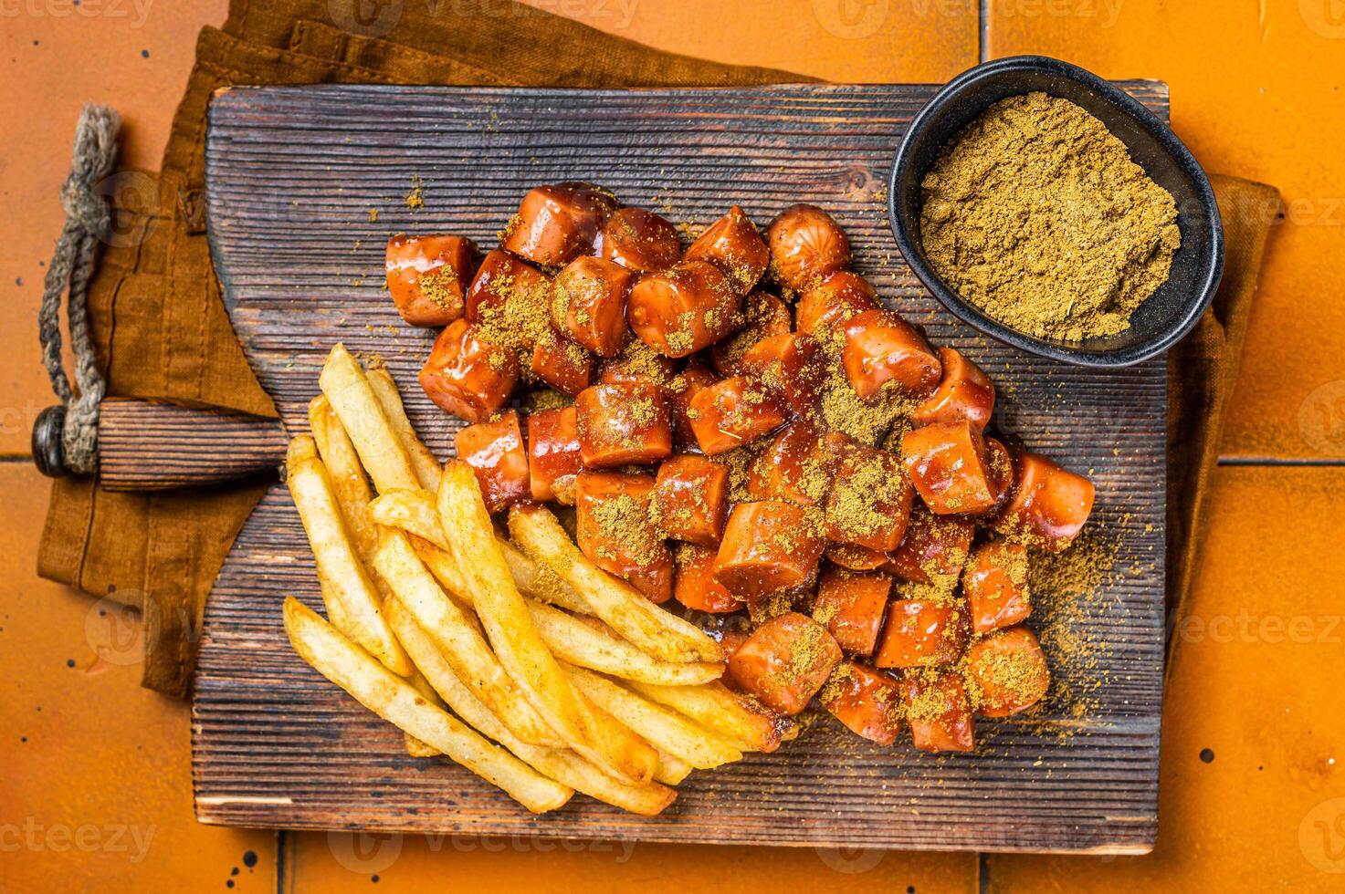 Curried sausage currywurst meal, curry wurst with french fry served on a wooden board. Orange background. Top view photo