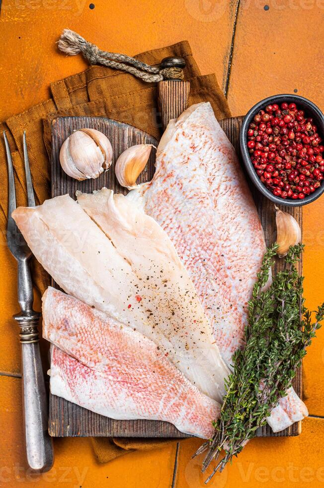 Uncooked ocean red perch fillet, redfish with herbs and spices. Orange background. Top view photo