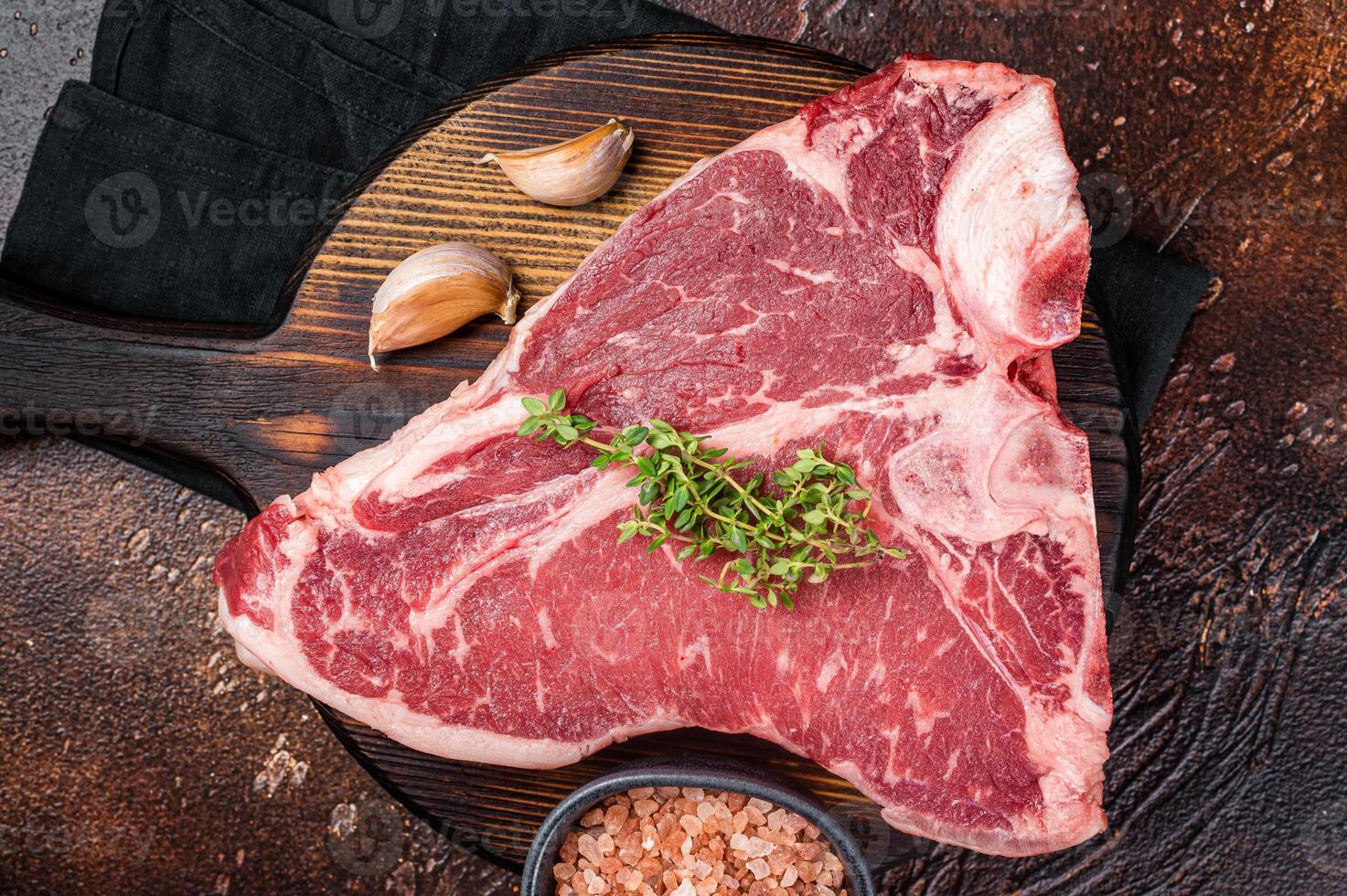 Raw Porterhouse steak, marbled beef meat on a wooden board. Dark background. Top view photo
