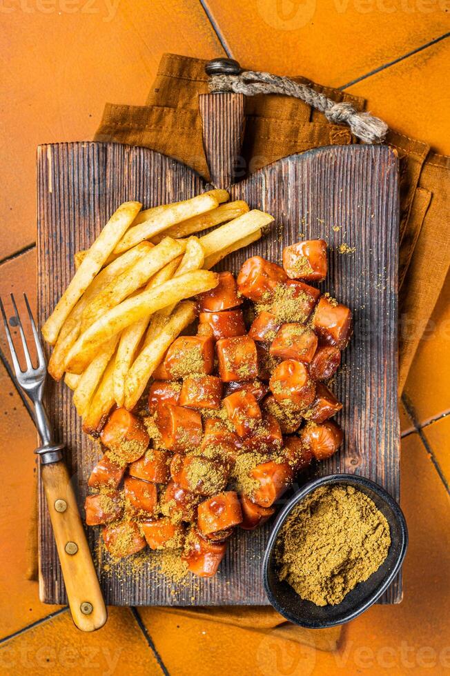 Curried sausage currywurst meal, curry wurst with french fry served on a wooden board. Orange background. Top view photo