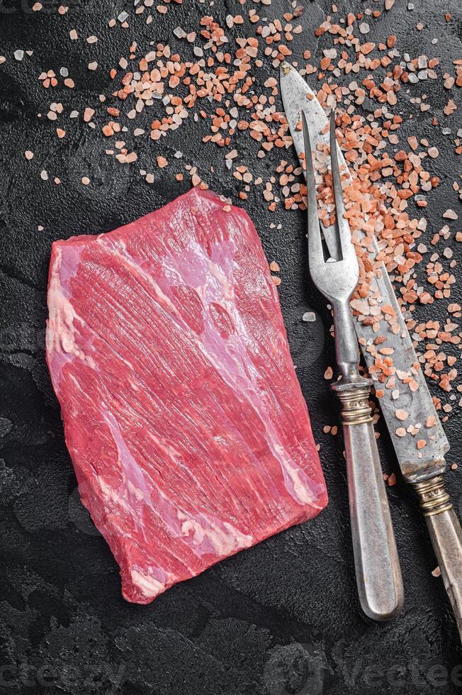 Uncooked Raw flap flank beef meat steak on kitchen table. Black background. Top view photo
