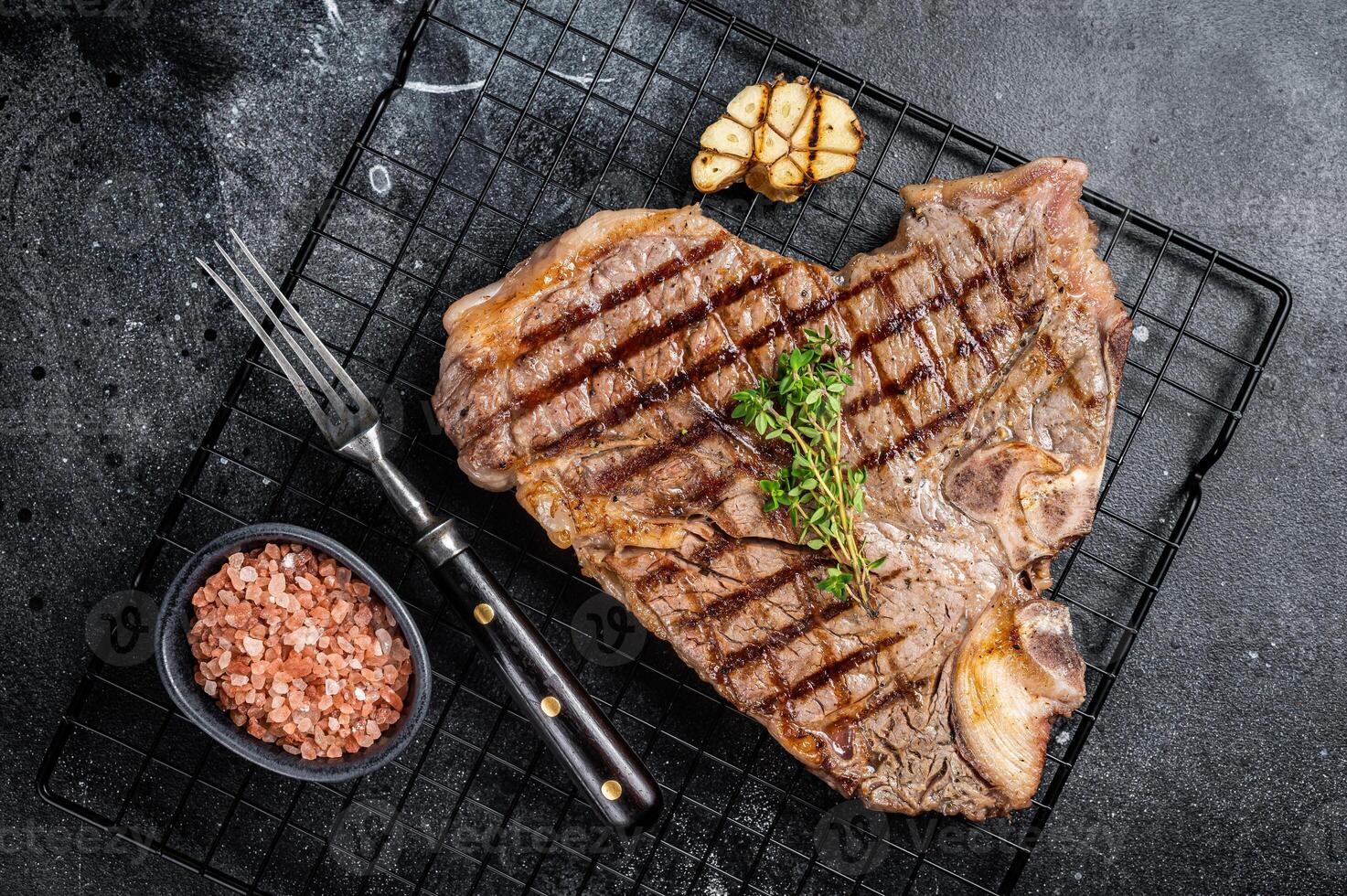 Grilled T-bone or Porterhouse beef meat Steak on a rack. Black background. Top view photo