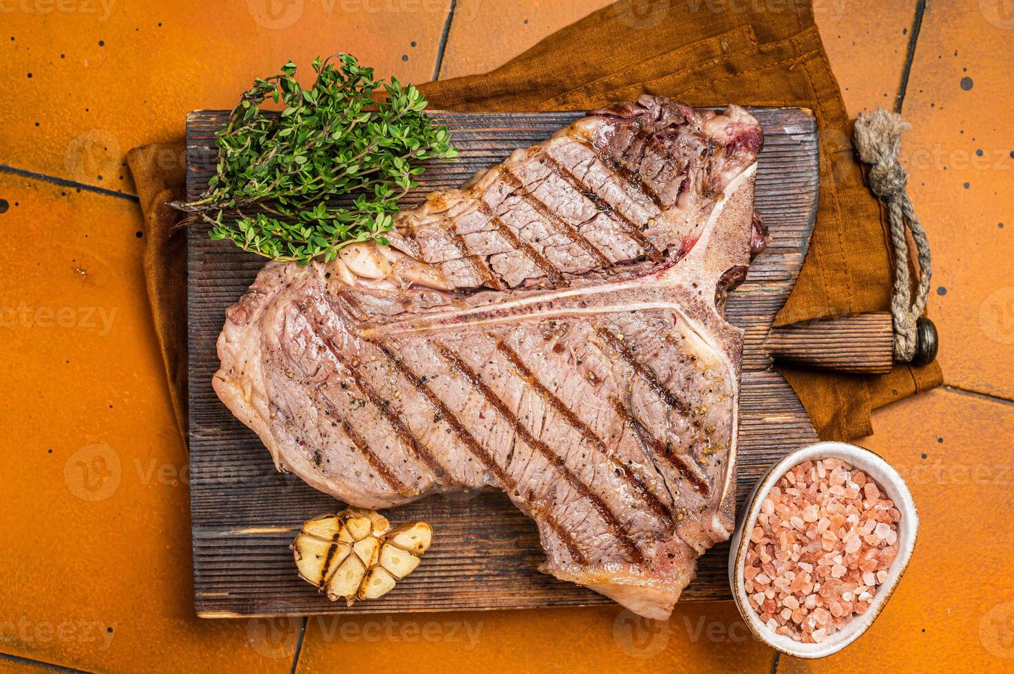 BBQ Roast T bone or Porterhouse beef meat Steak on a wooden board with spices. Orange background. Top view photo