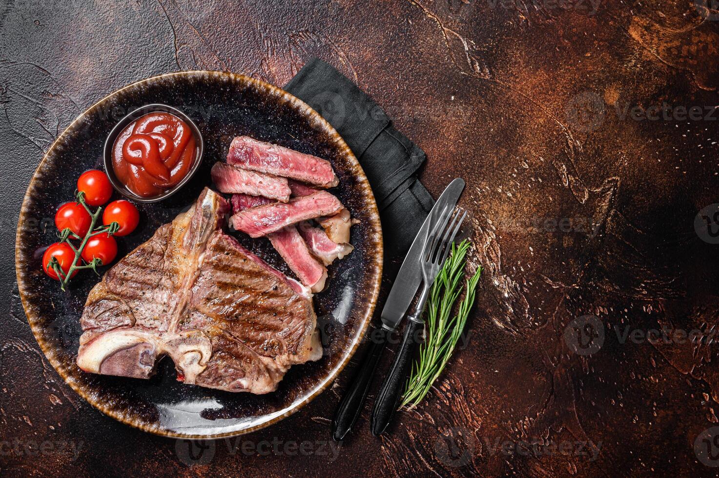 Grilled porterhouse beef meat Steak, cooked t bone in a plate with tomato. Dark background. Top view. Copy space photo