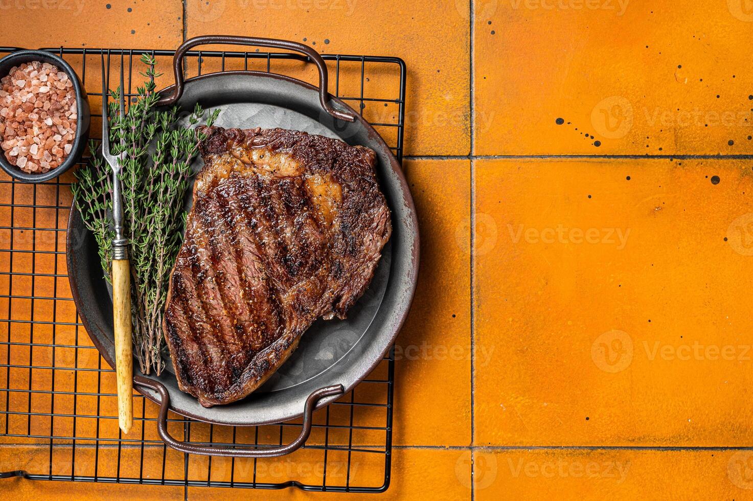 BBQ Grilled wagyu Rib Eye beef meat steak with herbs in steel tray. Orange background. Top view. Copy space photo