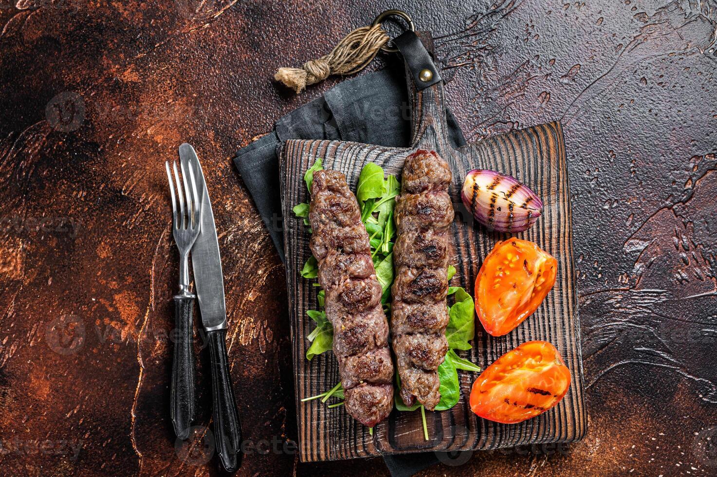 Turkish adana kebab, ground beef and lamb meat grilled on skewers served with tomato, salad and onion. Dark background. Top view photo