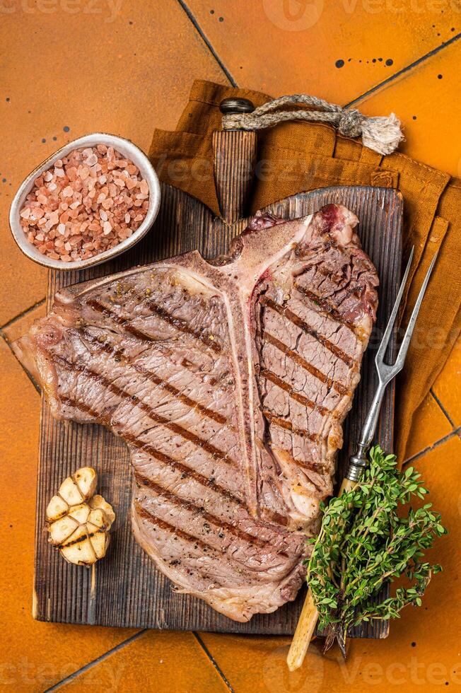 BBQ Roast T bone or Porterhouse beef meat Steak on a wooden board with spices. Orange background. Top view photo