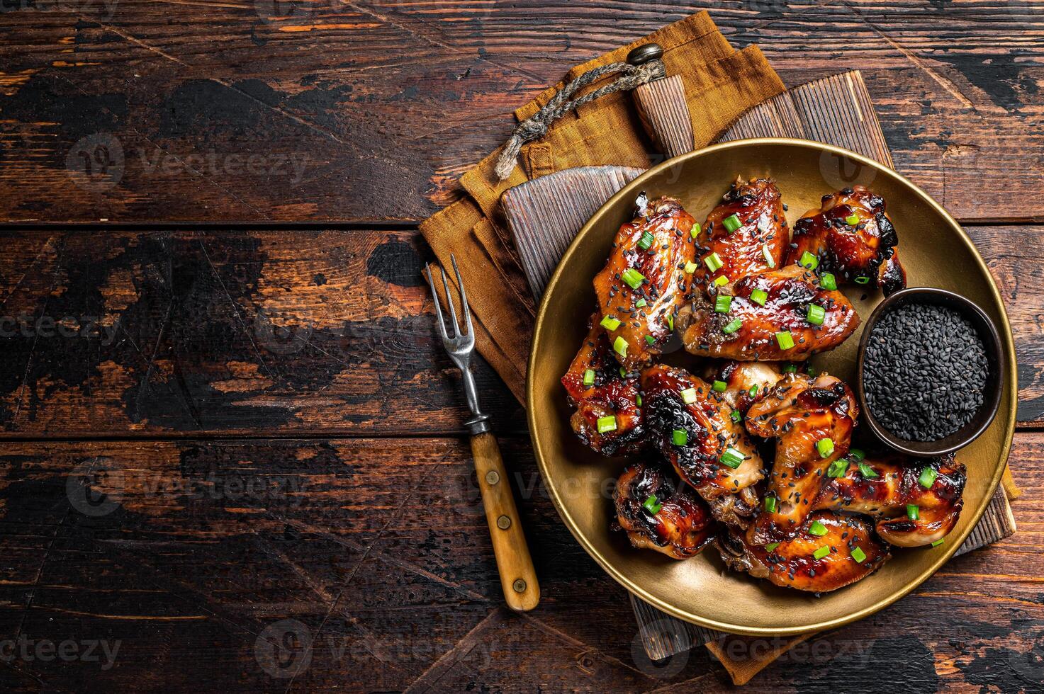 Teriyaki chicken wings with black sesame in a plate. Wooden background. Top view. Copy space photo