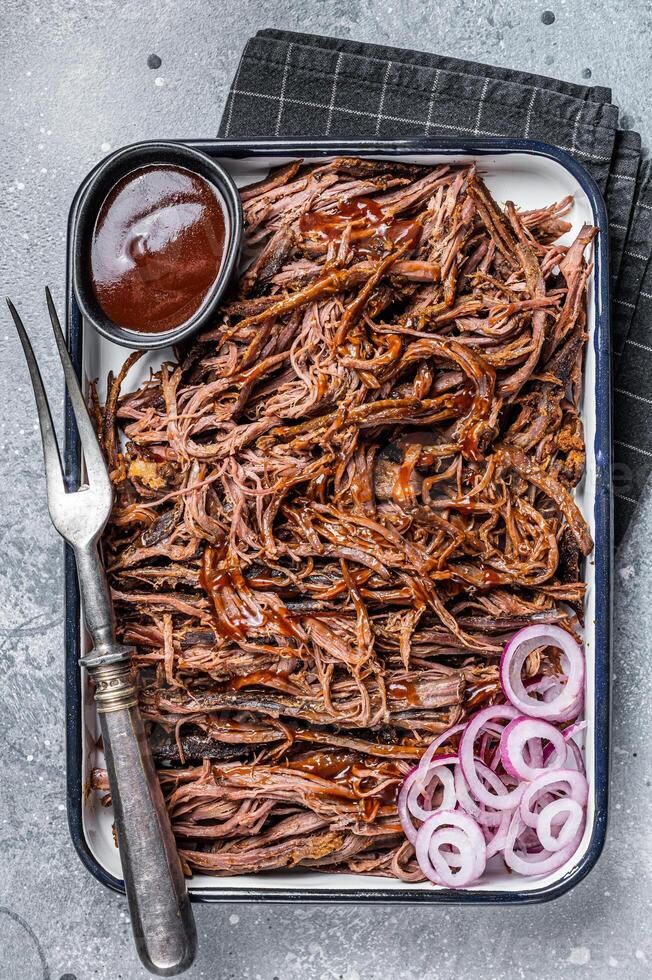 Pulled beef meat with hot chili sauce in baking dish. Gray background. Top view photo