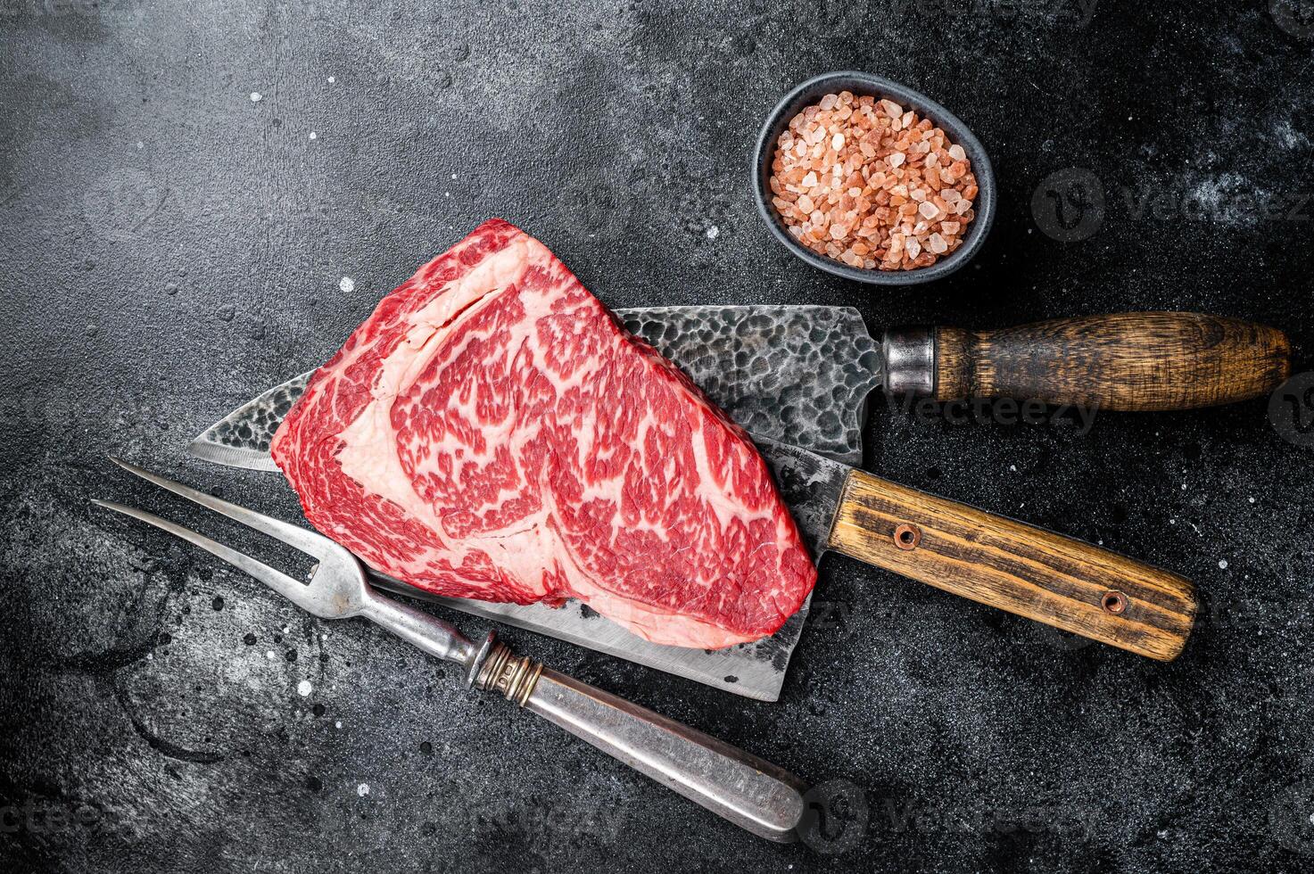 Butcher table with wagyu Rib Eye steak, raw beef meat. Black background. Top view photo