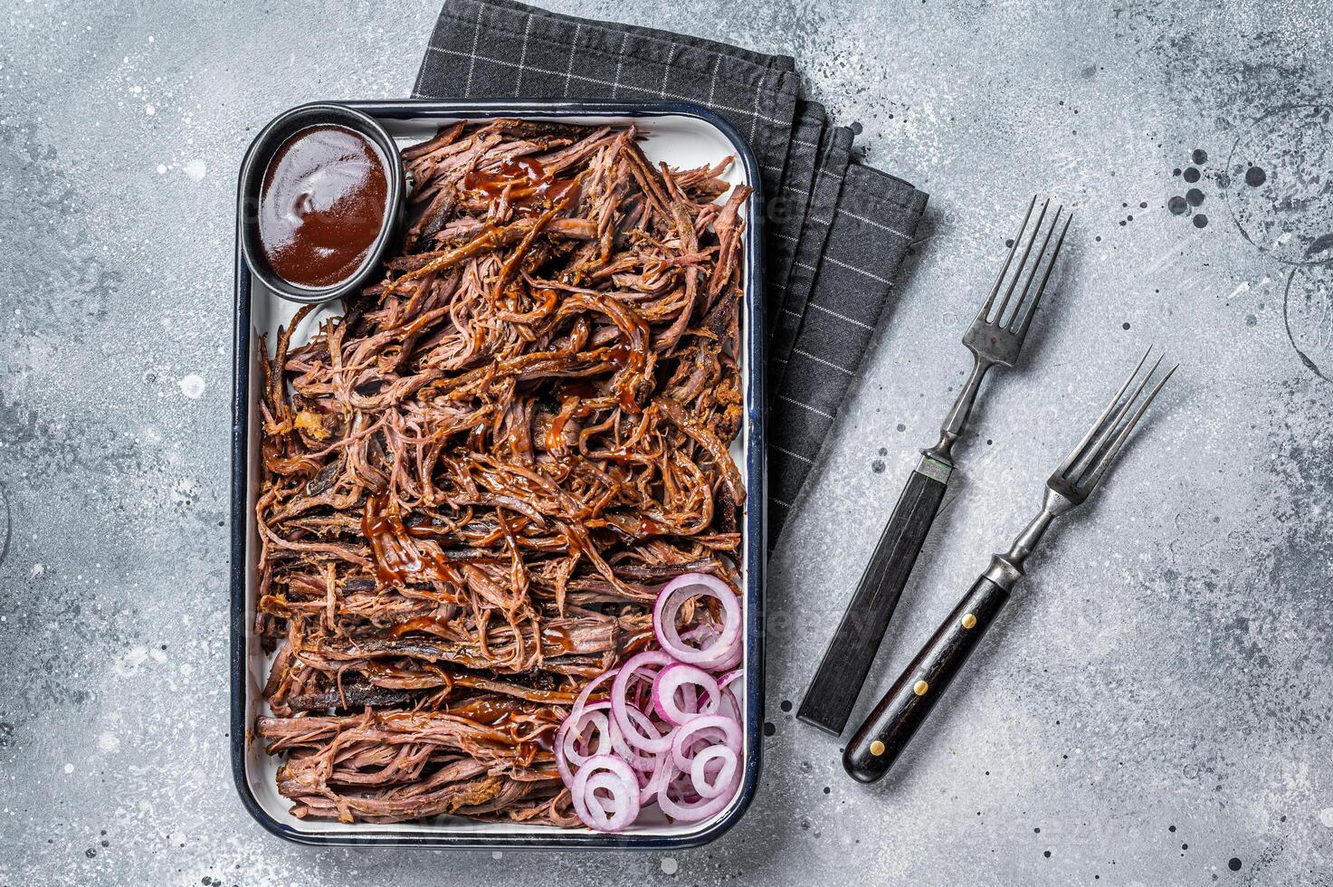 Pulled beef meat with hot chili sauce in baking dish. Gray background. Top view photo