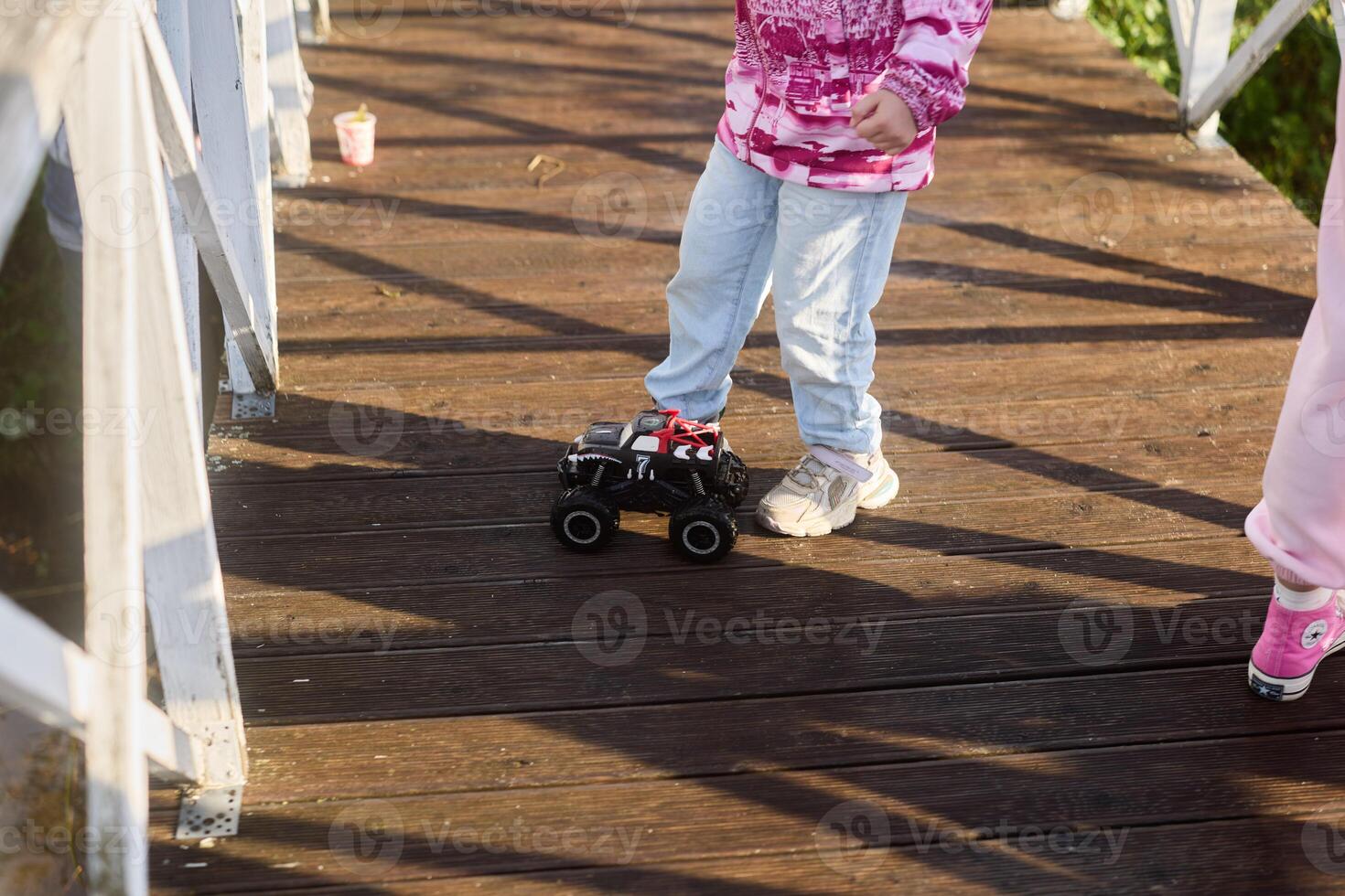 A playful child joyfully maneuvering a remotecontrolled truck while standing on a bridge photo
