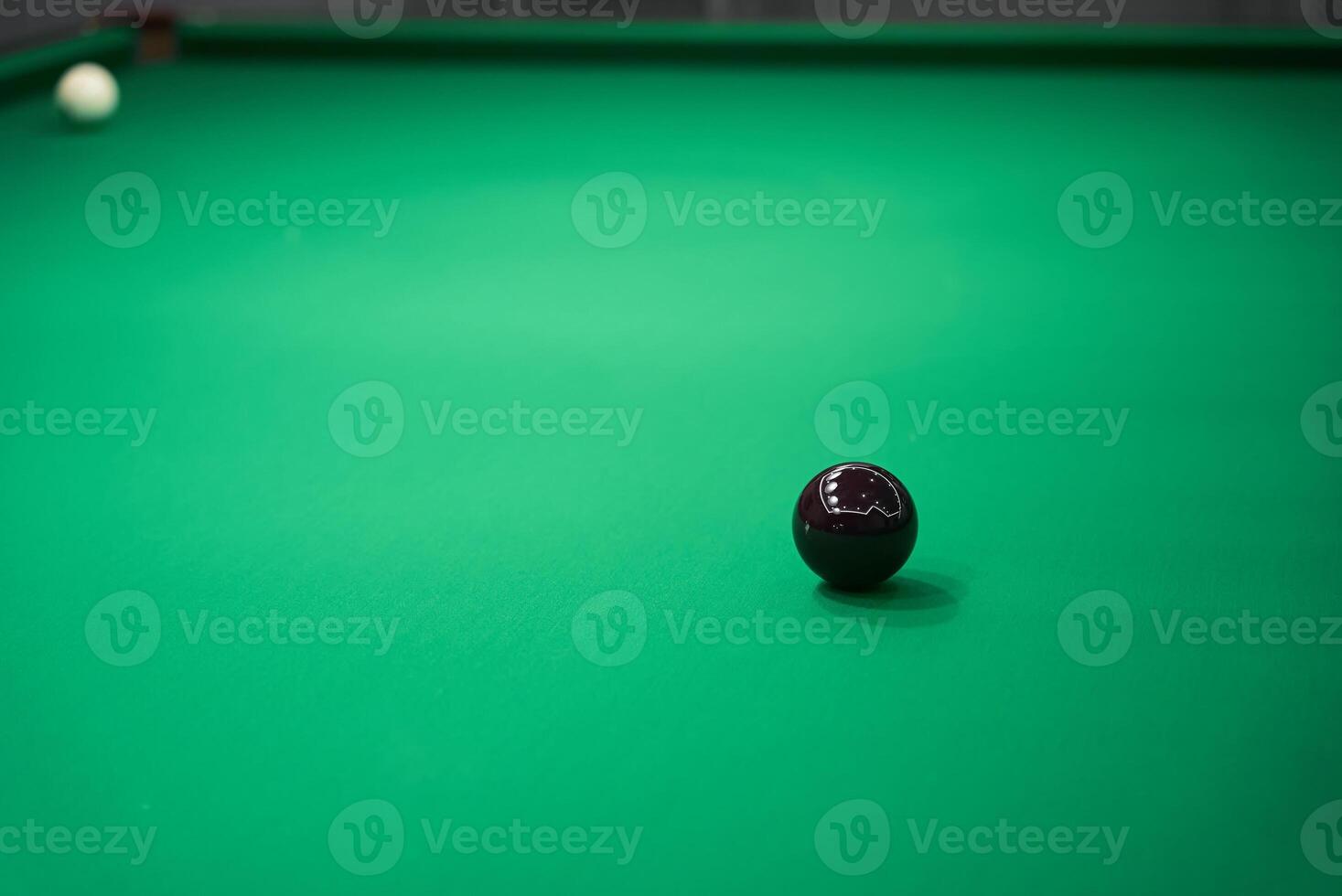 A Detailed CloseUp View of a Black Ball Resting on a Luxurious Green Billiard Table photo