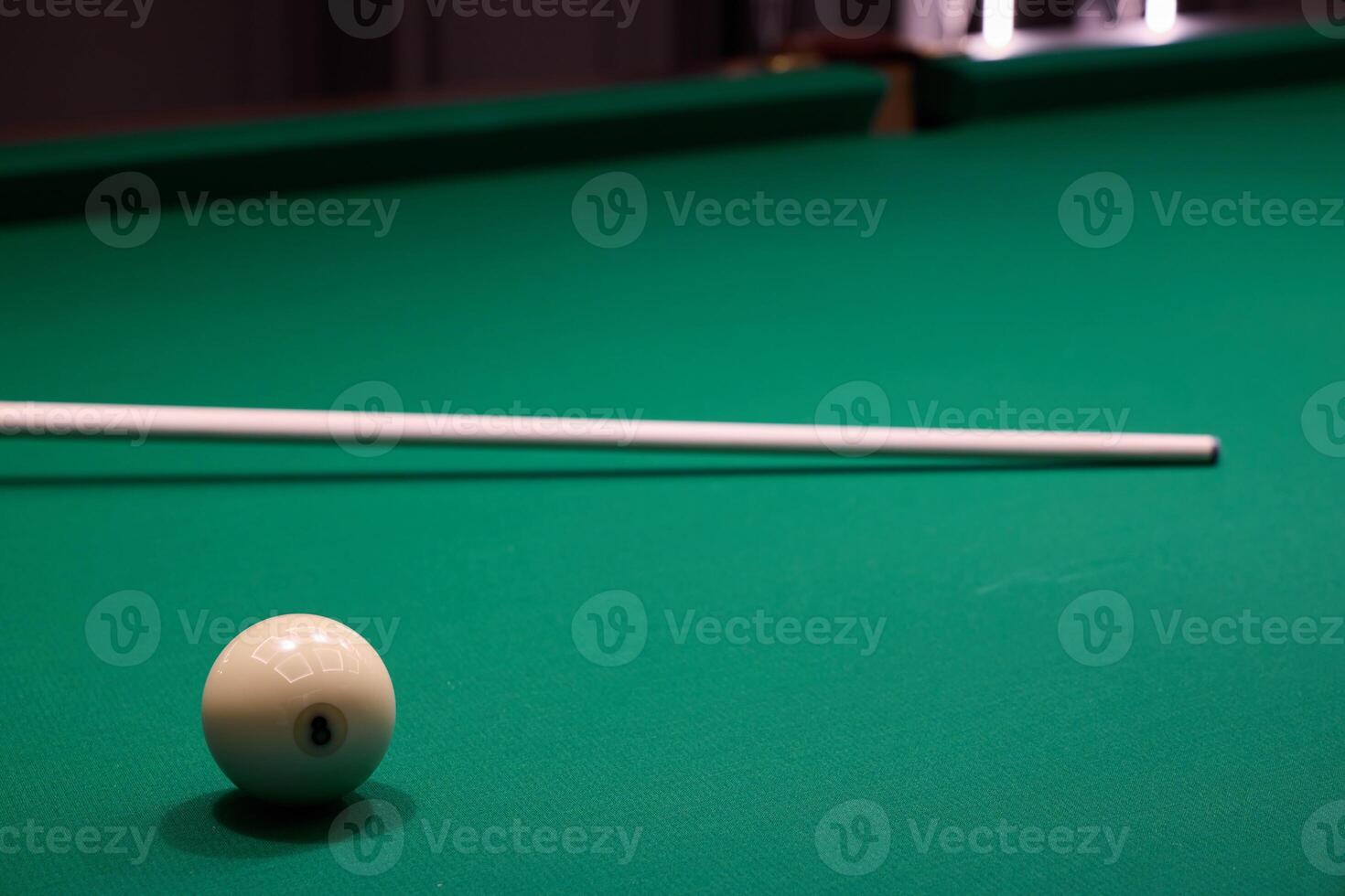 A white cue ball on a green felt pool table, with a cue stick nearby for the next shot photo