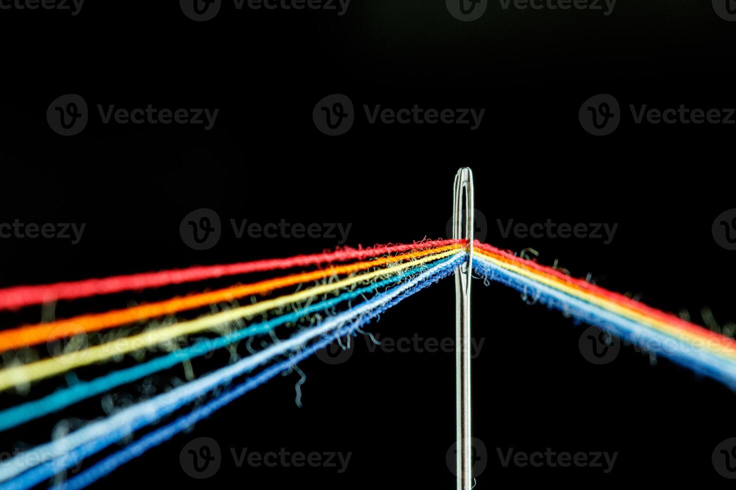 multi-colored threads for sewing in the form of a rainbow pass through an antique needle on a black background photo