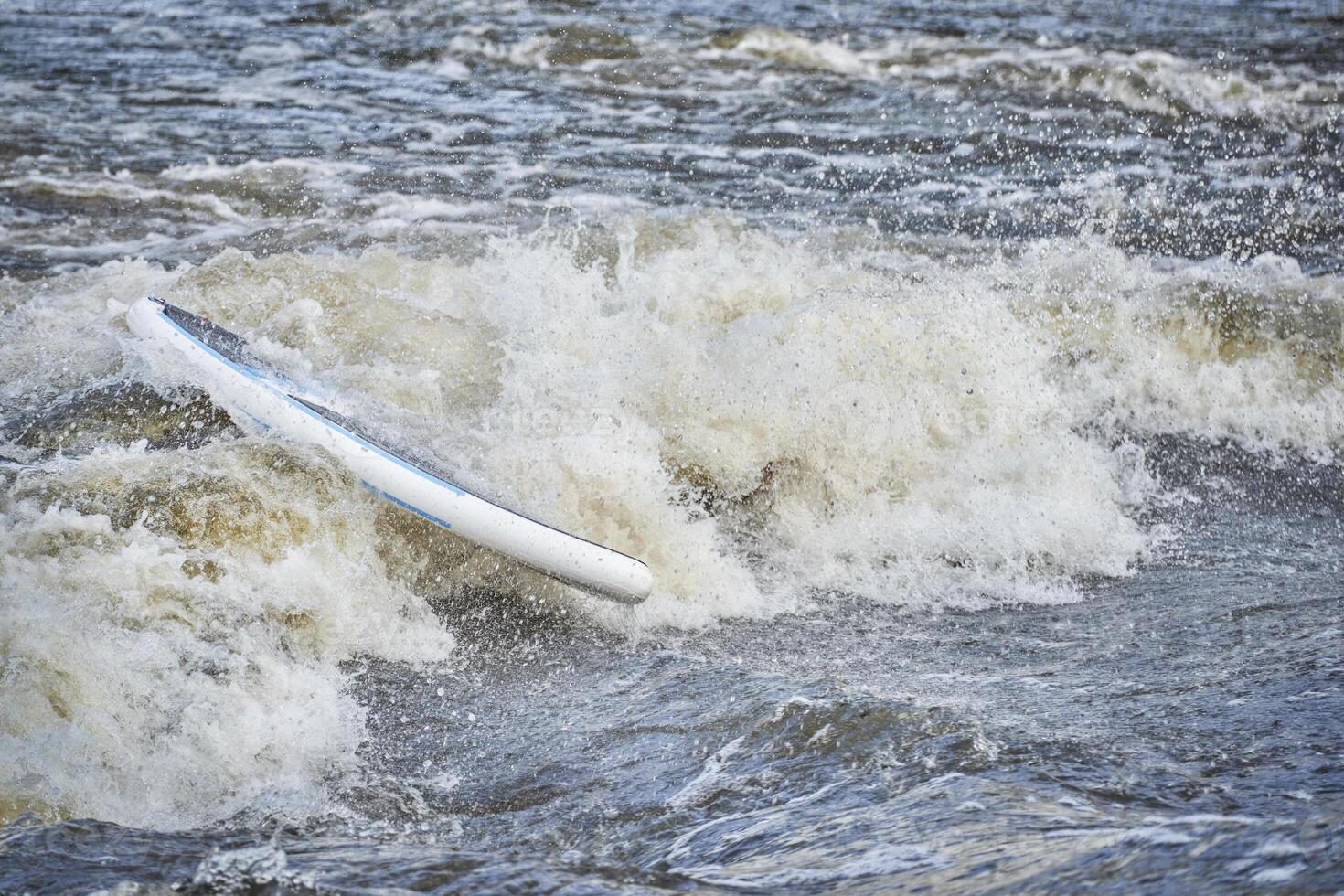 stand up paddleboard with a paddler under water in a rapid photo