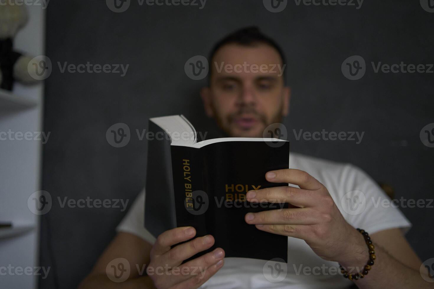 A 30-year-old man with a Bible attends an online church service, talks with the pastor photo