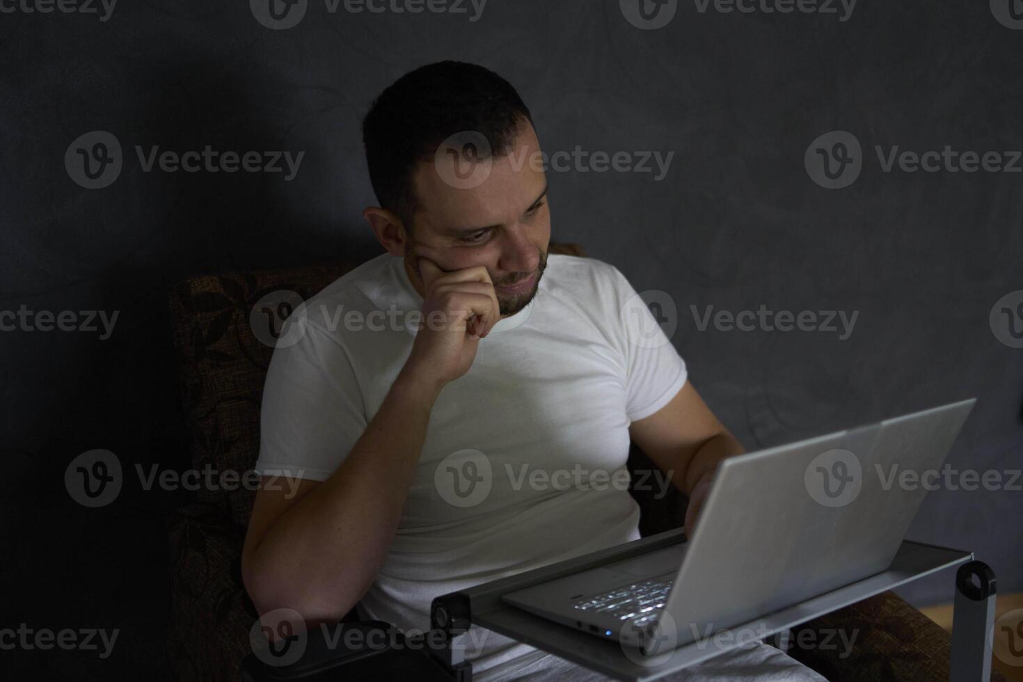 A 30-year-old man is stressed while working on a laptop from his home office photo