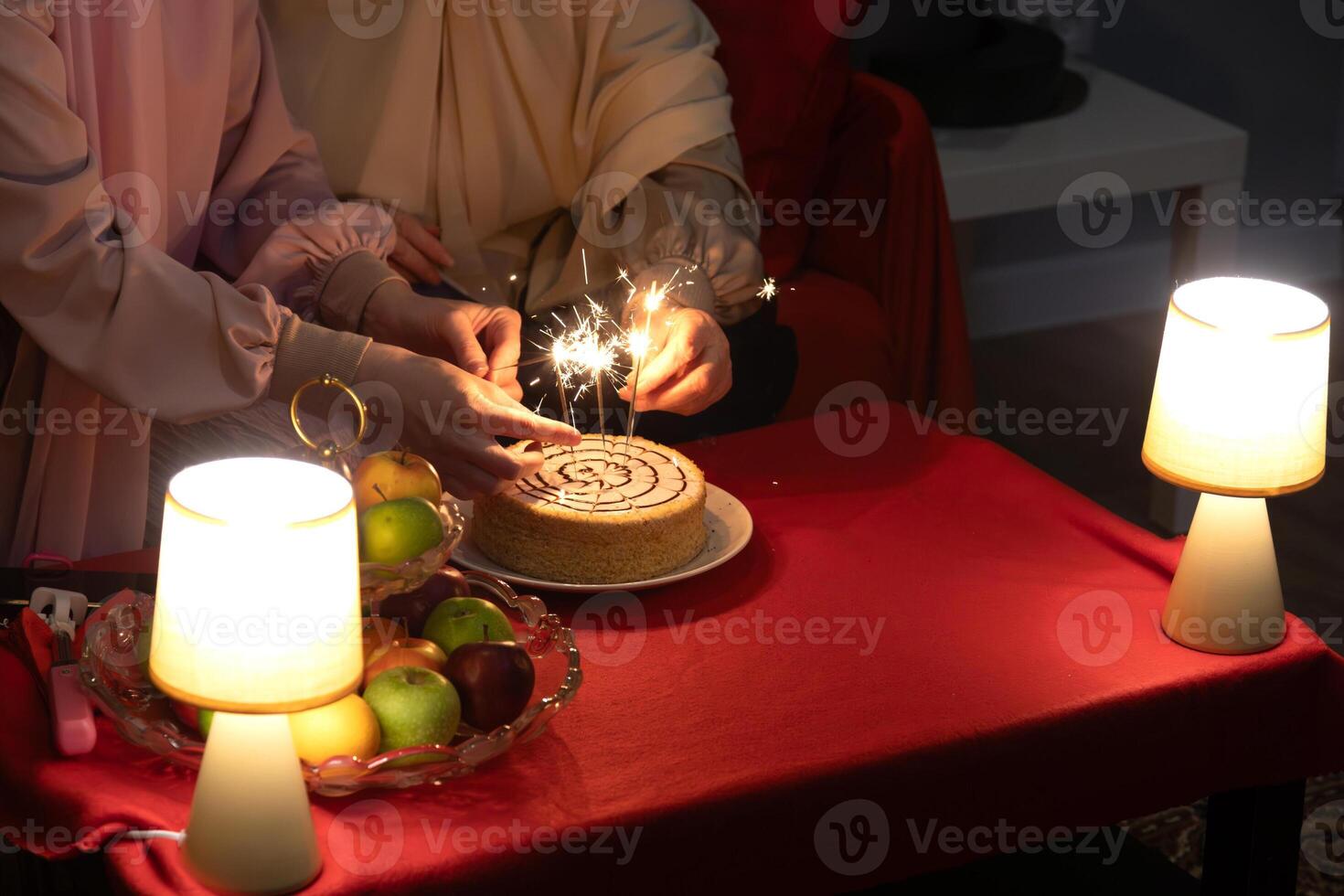 Women celebrate with cake and fireworks at cafe, ignite sparklers on birthday cake, closeup of hand, space for text. photo