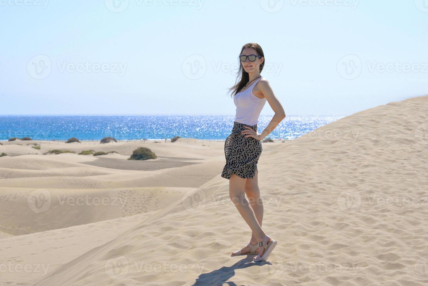 A girlstanding in a model pose on the sand at the background of the sea. Dune in Maspalomas, Gran Canaria. Touristic travel concept photo
