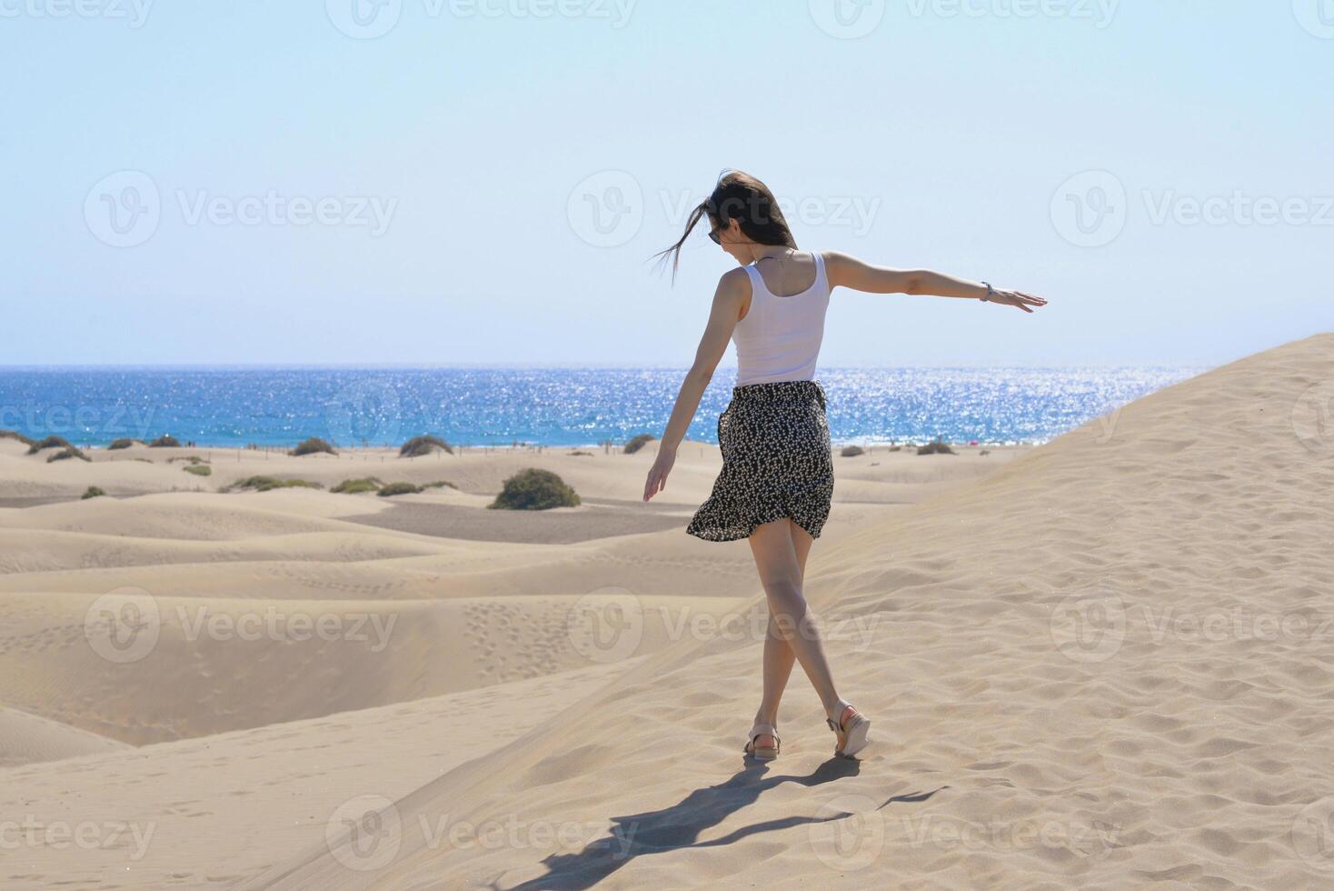 A girl walks along the sand against the background of the sea, rear view. Dune in Maspalomas, Gran Canaria. Touristic travel concept photo