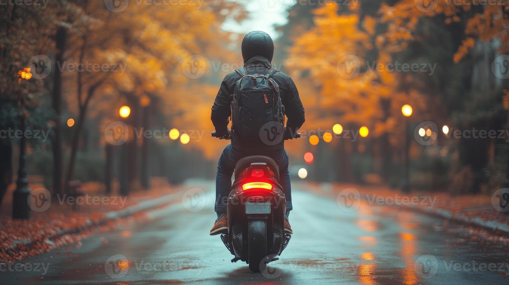 A person on a motorcycle travels along a wet street surrounded by autumn foliage and soft evening lights photo