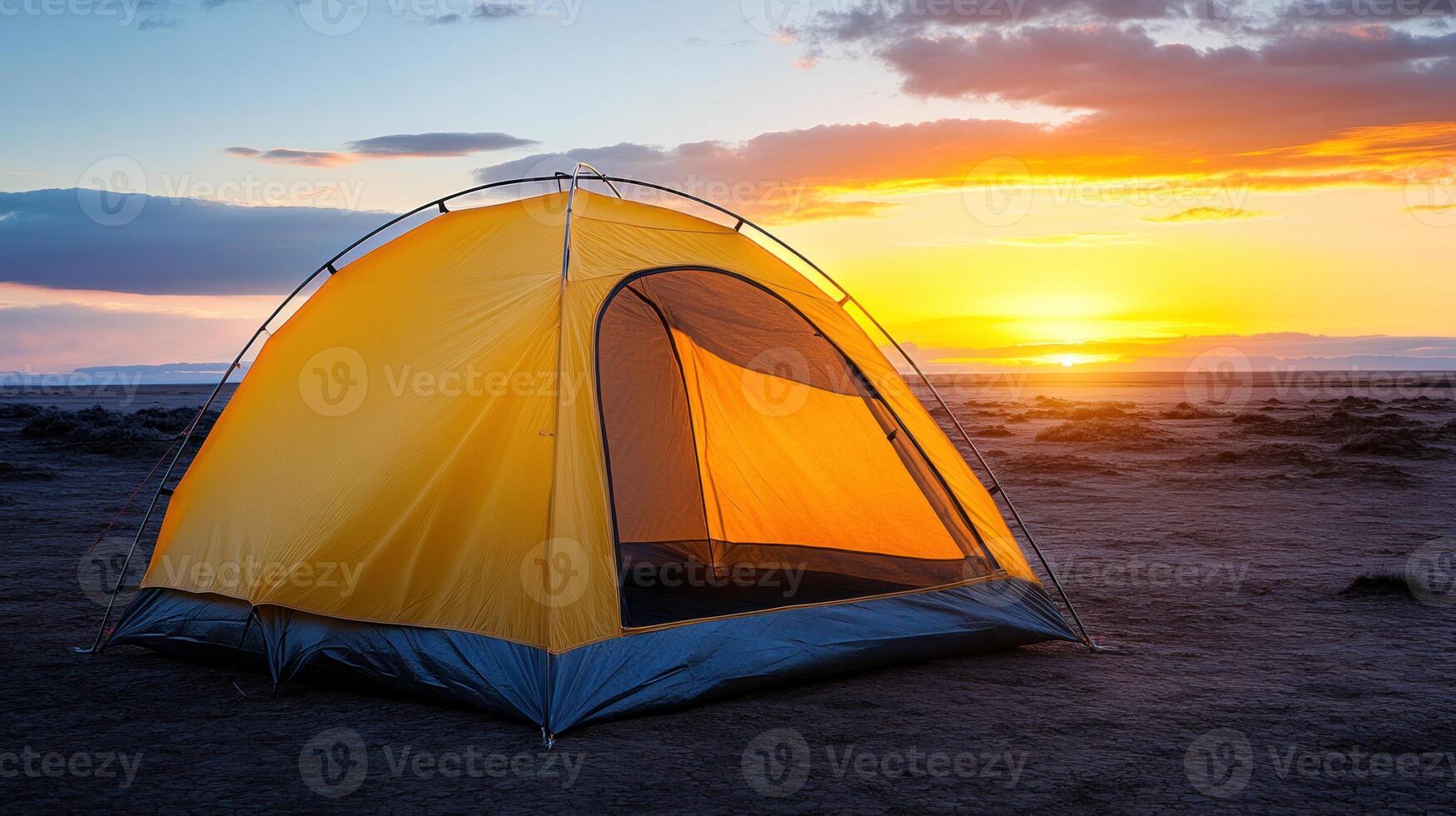A yellow tent glows warmly as the sun sets, casting colors across the open terrain in the evening light photo