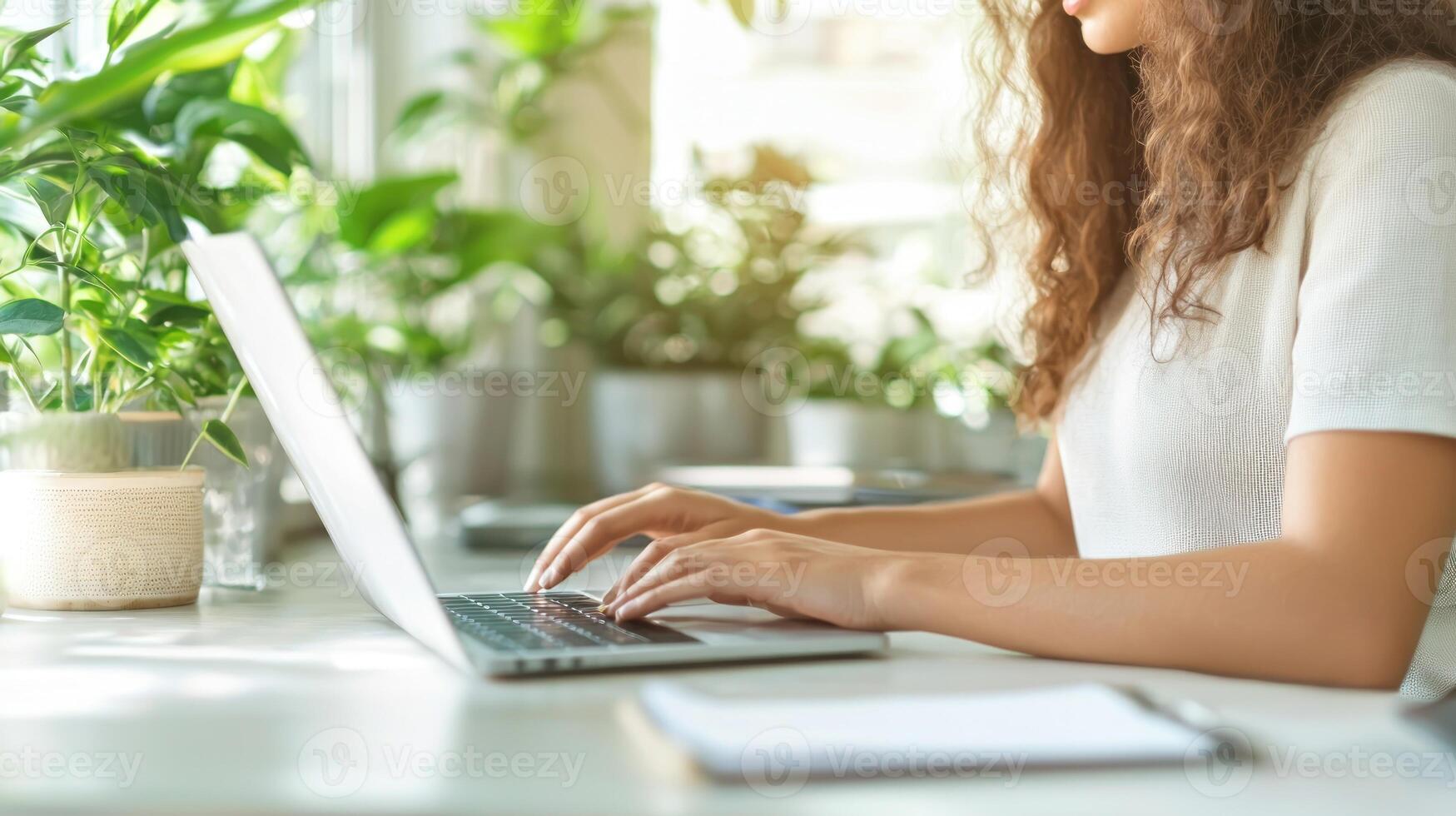 A person works on a laptop, surrounded by greenery and natural light filtering through the window photo