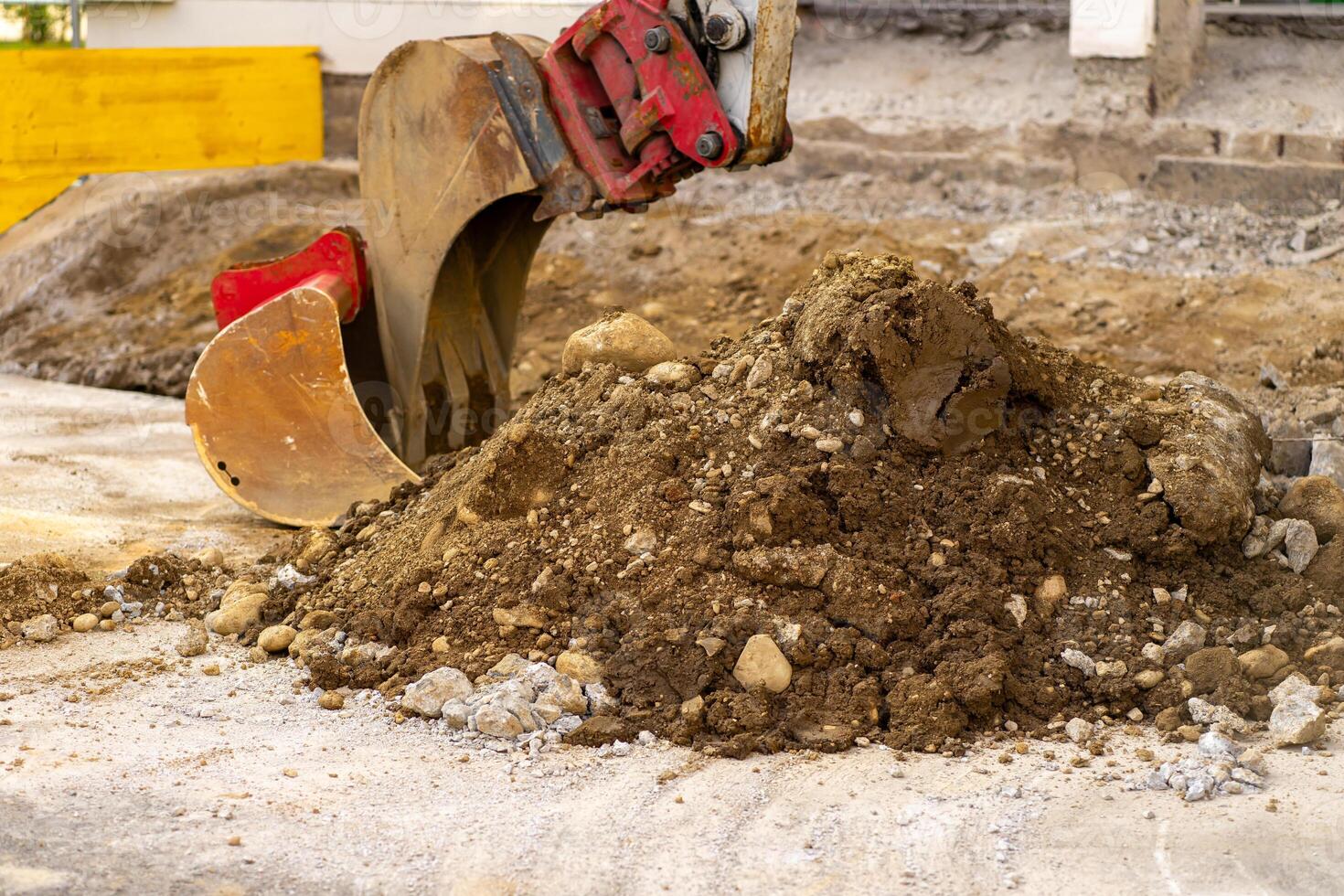 Excavator bucket collects soil and old asphalt at a construction site photo