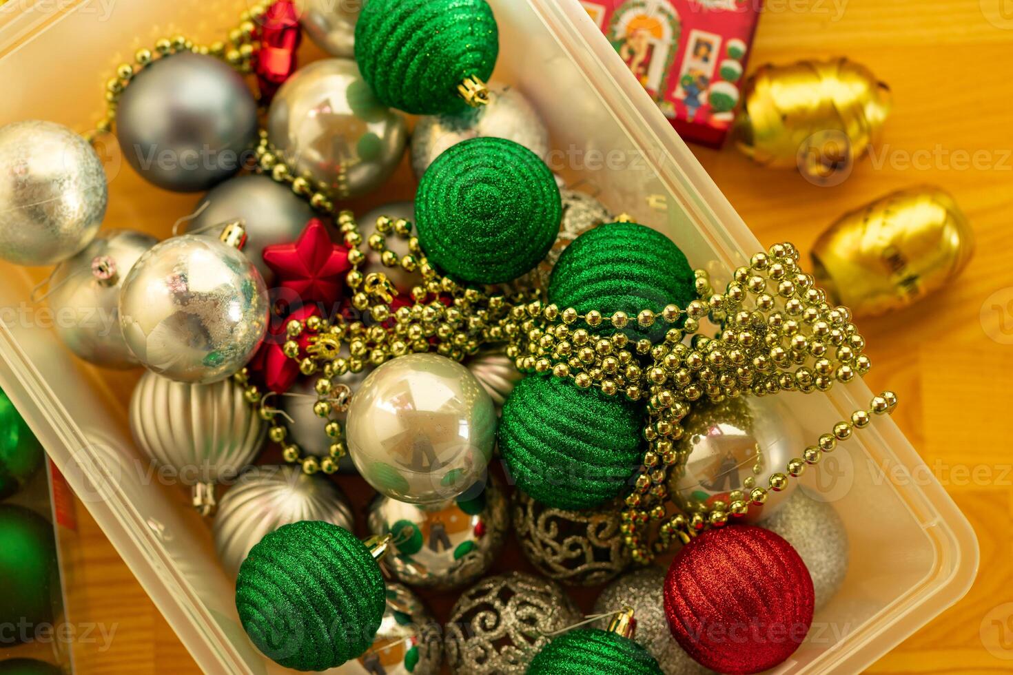 Multi-colored Christmas tree toys and garlands in a plastic box on the floor photo
