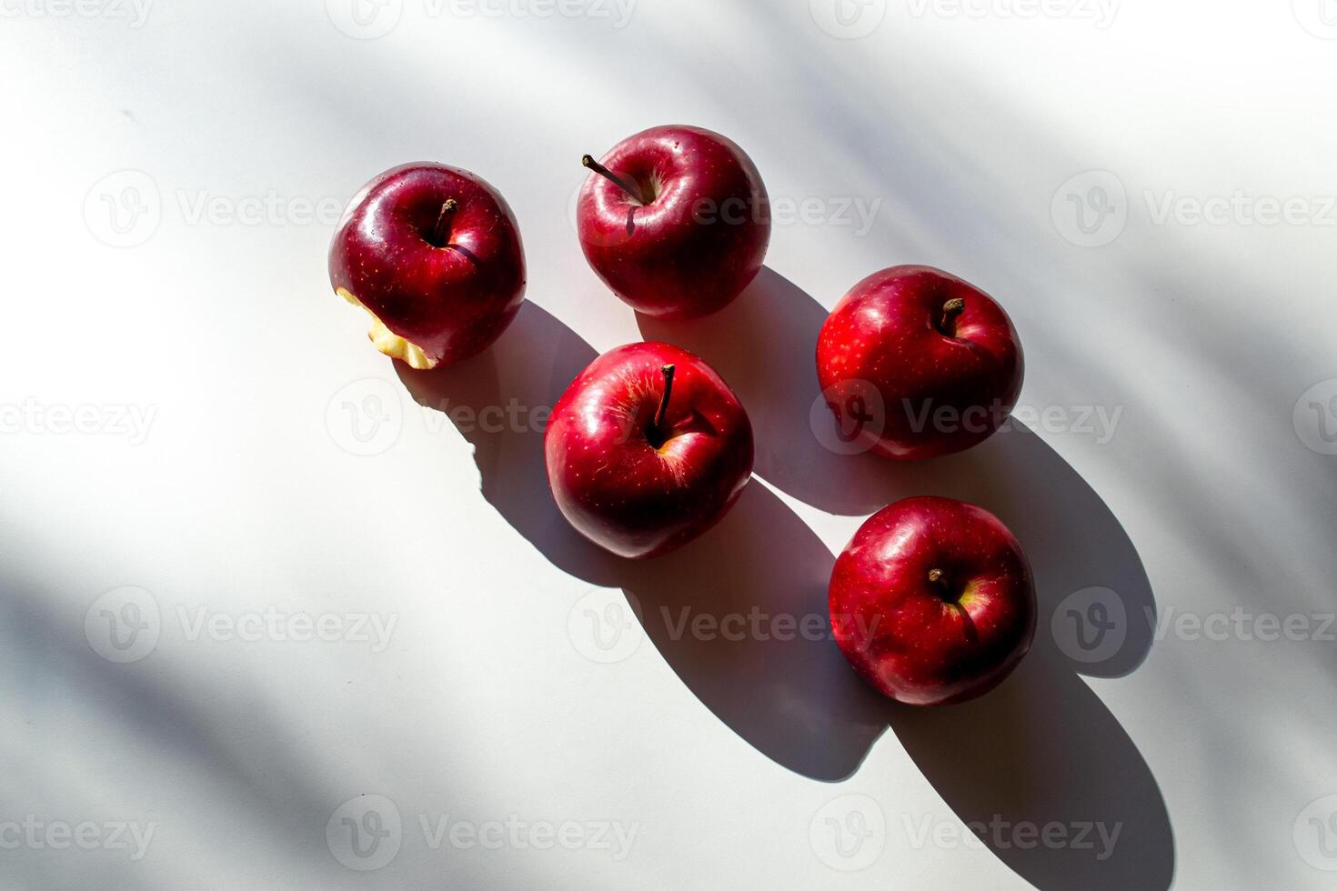 Five red ripe apples lying on a white table and their shadows photo